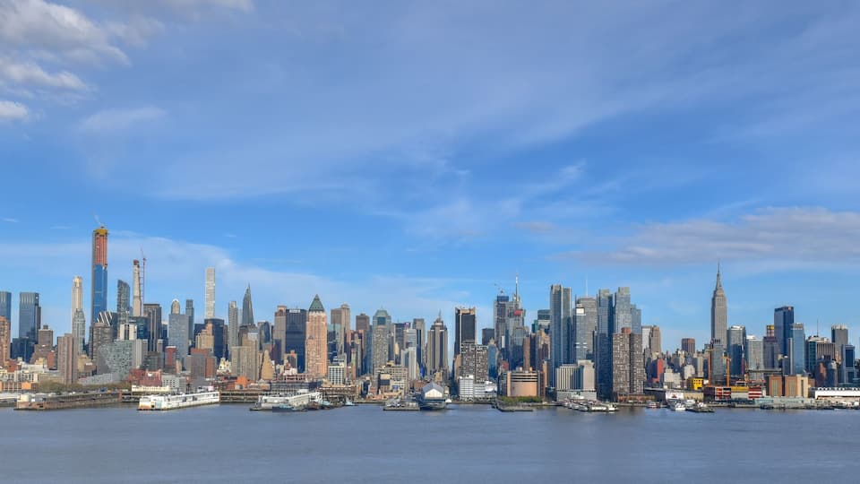A city skyline with numerous skyscrapers and a body of water in the foreground.