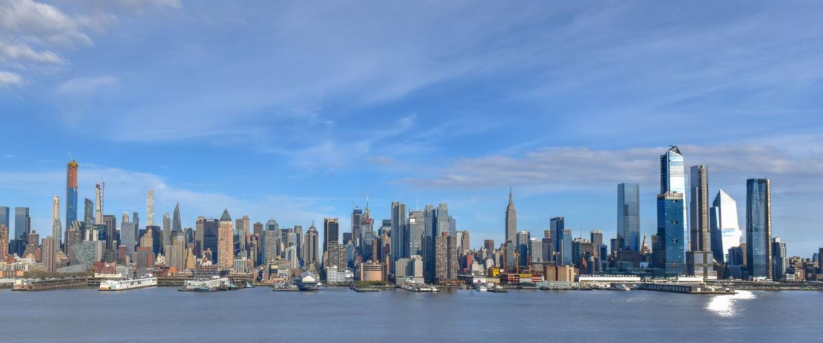 A city skyline with numerous skyscrapers and a body of water in the foreground.