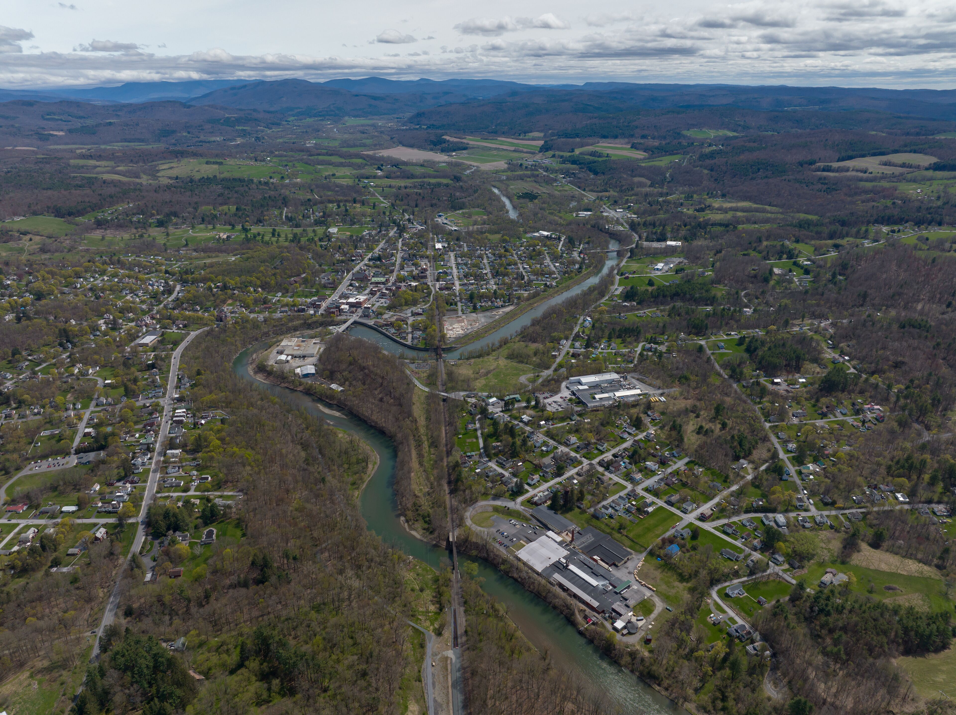 An aerial view of a town with a river running through it, surrounded by hills and green fields.