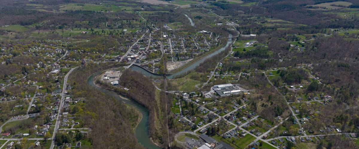 An aerial view of a town with a river running through it, surrounded by hills and green fields.