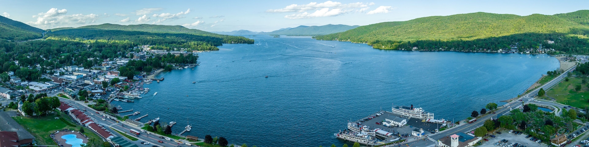 Un lago extenso rodeado de colinas y un pueblo con muelles y barcos.