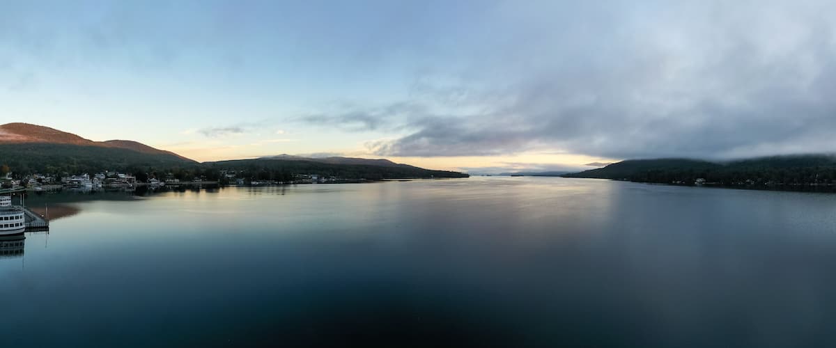 A calm lake with mountains in the background and a boat docked on the left.