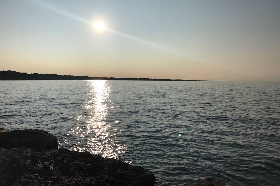Ett stilla hav med solljus som speglas i vattnet, en klippig kust och ett avlägset landområde.