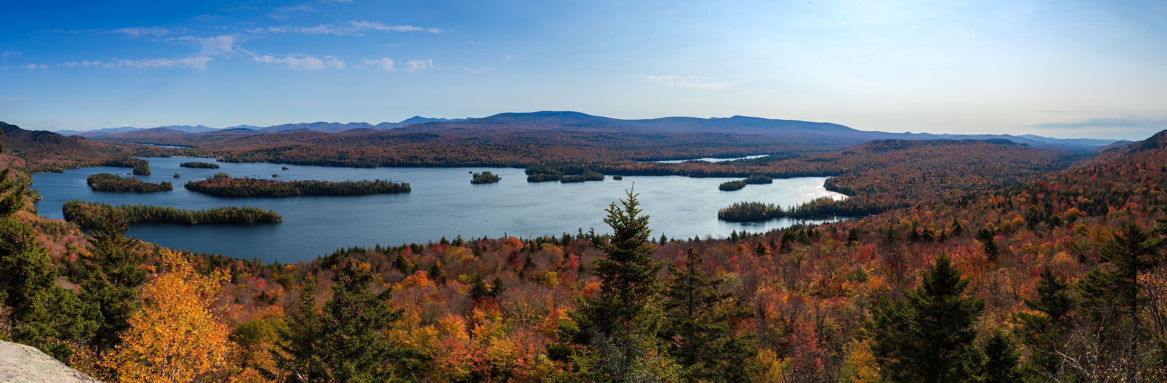 A lake surrounded by autumn-colored forests and distant mountains.