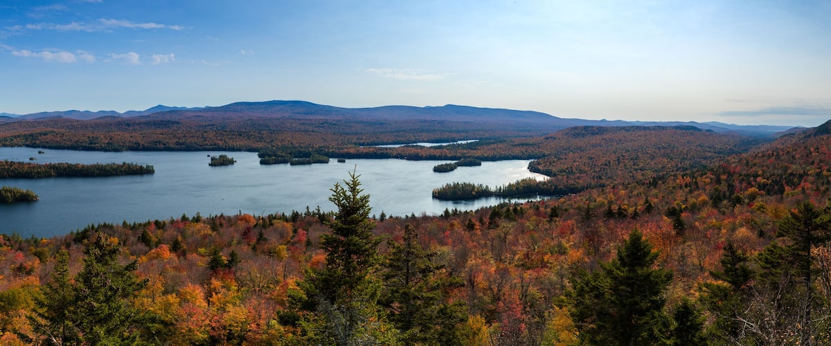 A lake surrounded by autumn-colored forests and distant mountains.