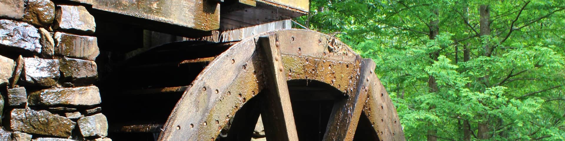 A large wooden water wheel attached to a brick structure, surrounded by lush green trees.