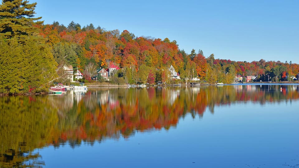 A calm lake reflecting colorful autumn trees and houses along the shore.