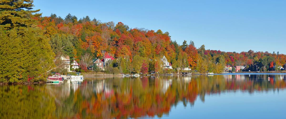 A calm lake reflecting colorful autumn trees and houses along the shore.