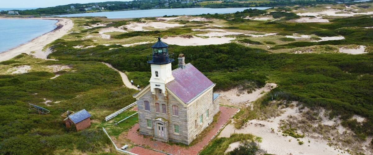 A lighthouse on a grassy dune with a beach and water in the background.