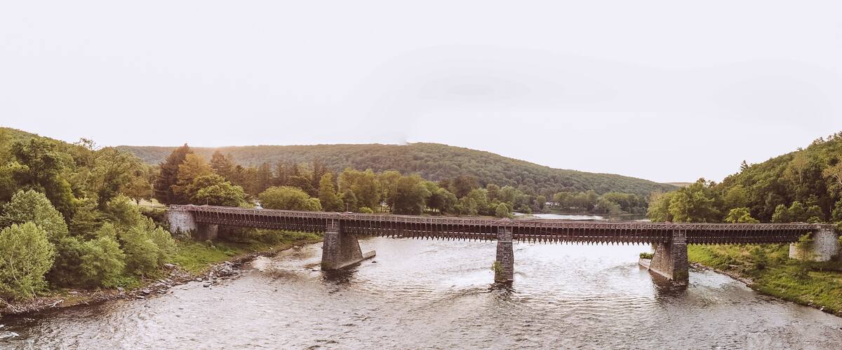 A stone bridge over a river, surrounded by lush greenery and hills.
