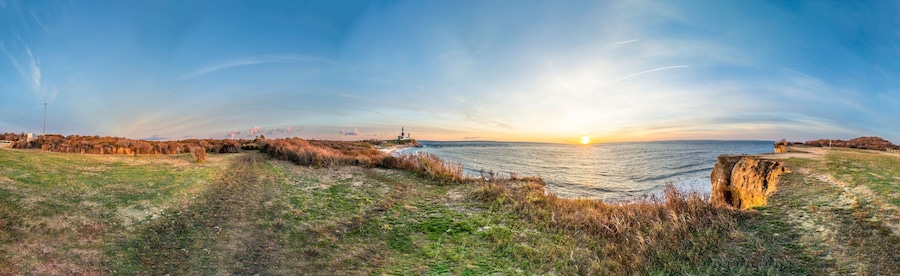 A coastal landscape with a sunset, grassy fields, and a cliff.