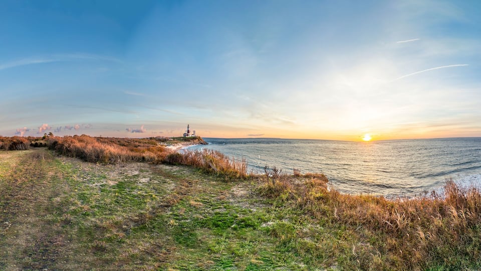 A coastal landscape with a sunset, grassy fields, and a cliff.
