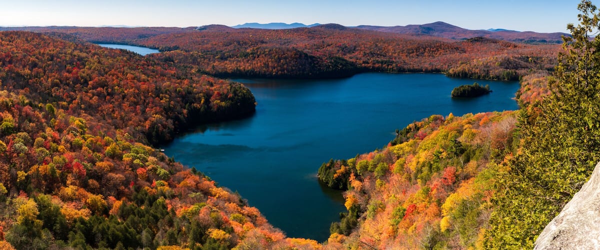 A mountainous landscape with a lake surrounded by autumn-colored trees.