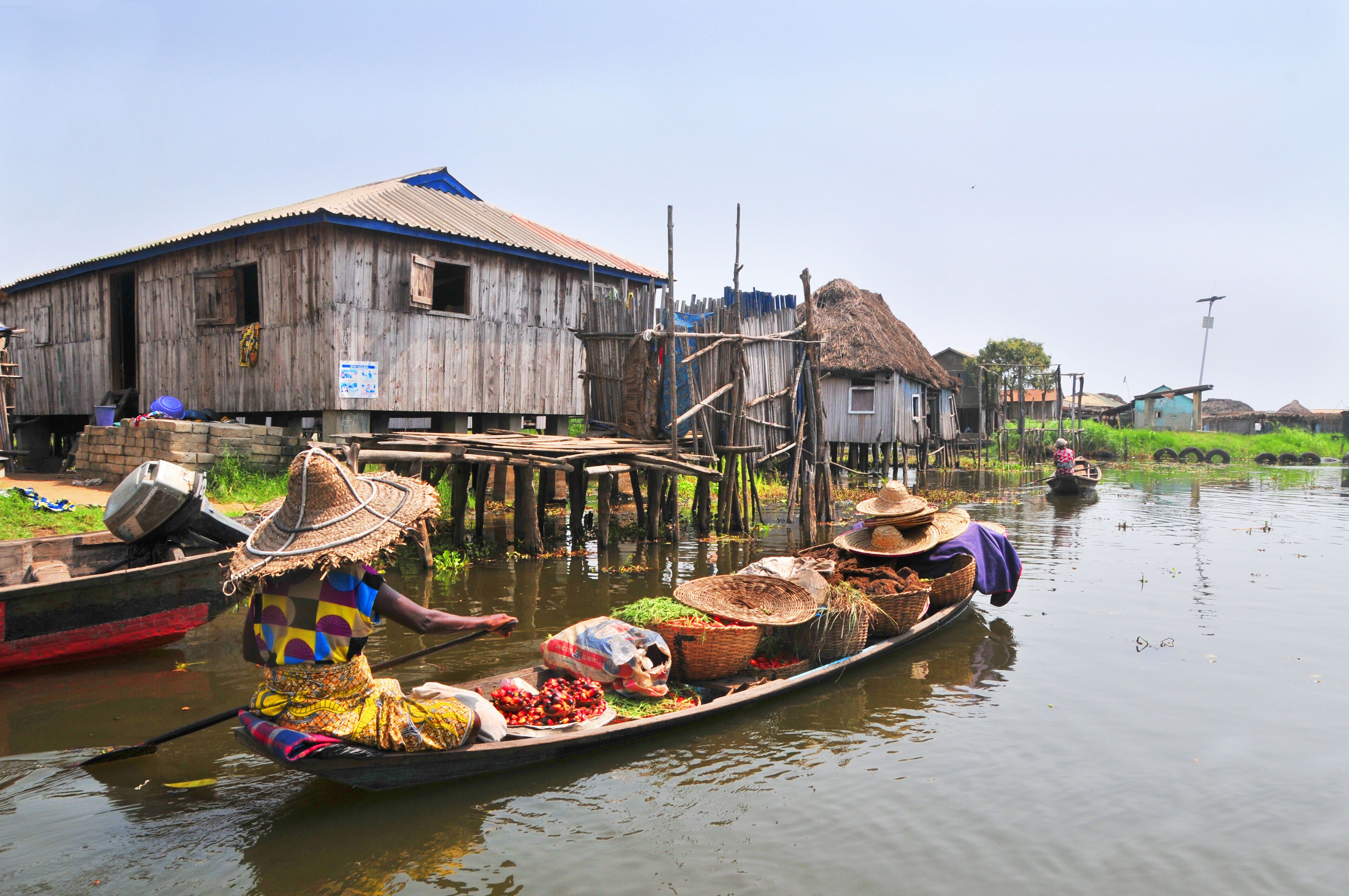 A wooden house with a blue roof, a thatched-roof structure, and a wooden dock extending into the water.