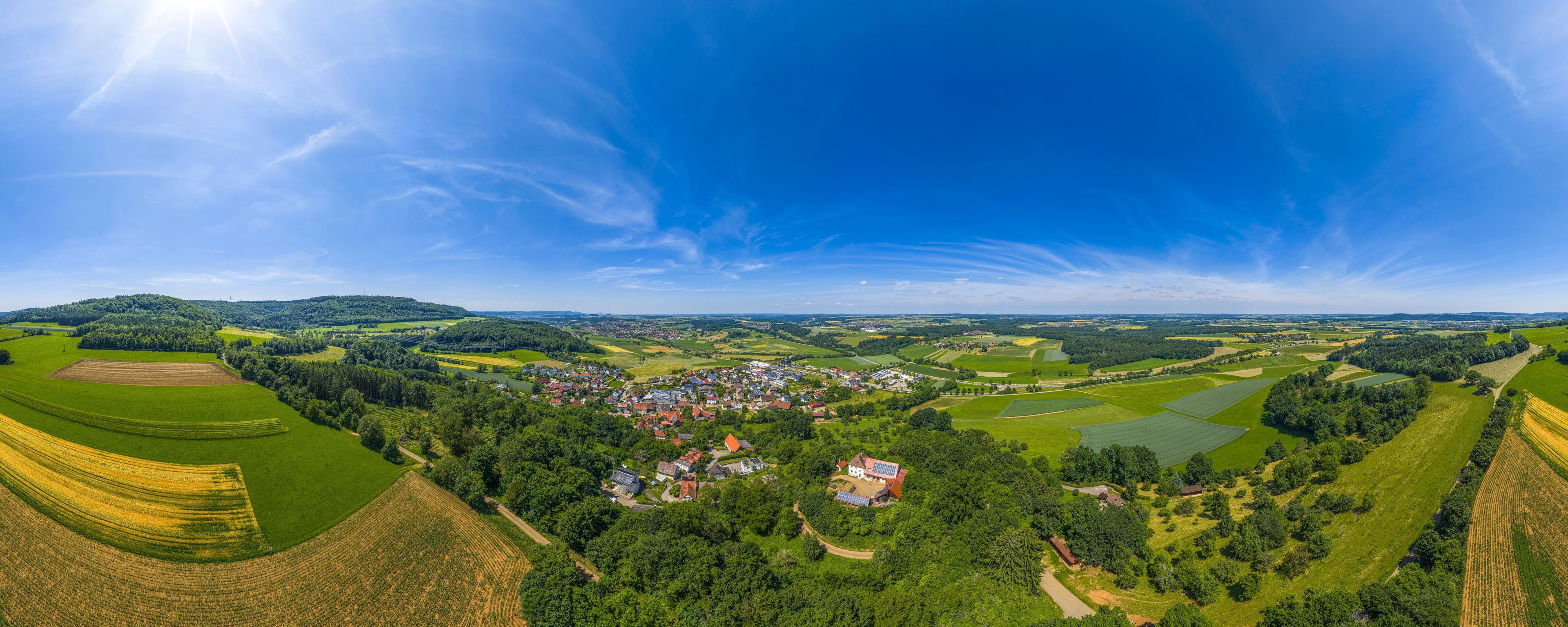 A panoramic view of a rural landscape with a village, rolling green fields, and distant hills.