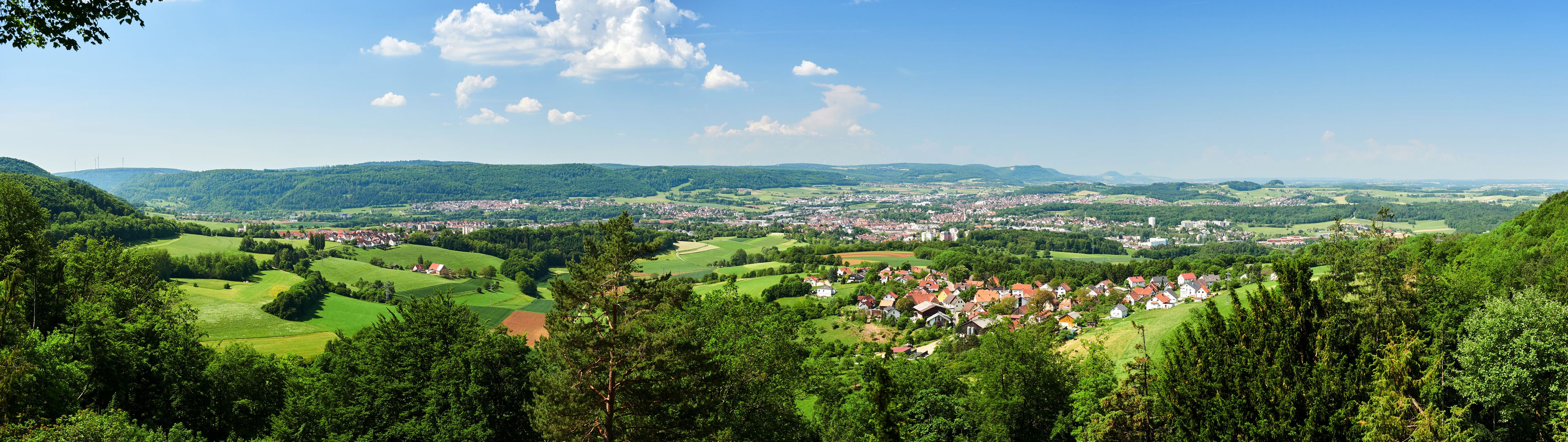 A panoramic view of a town nestled in a valley with surrounding hills and greenery.