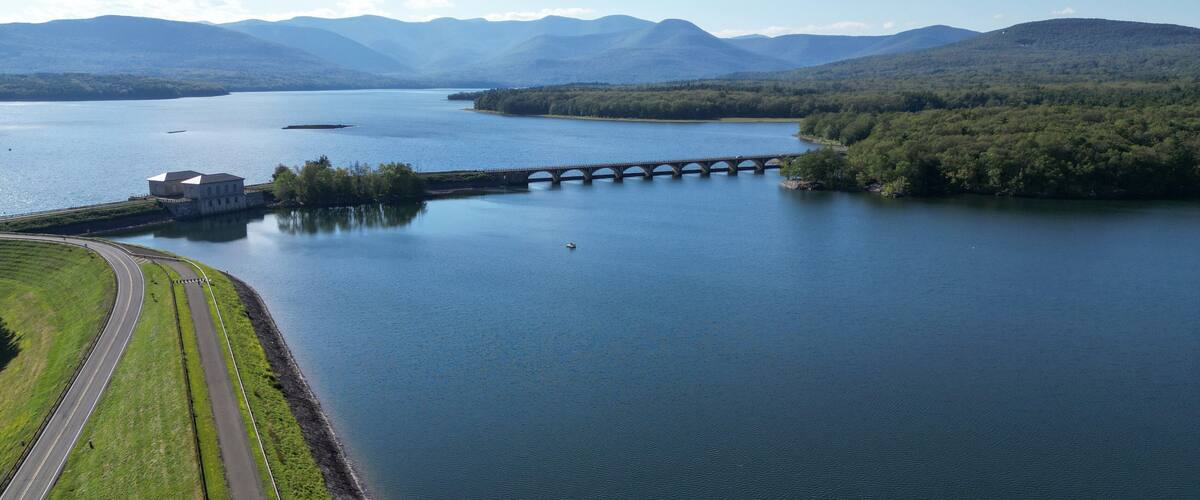 A large lake with a bridge, surrounded by mountains and greenery.
