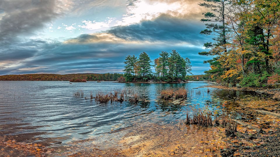 A calm lake surrounded by trees with autumn foliage.