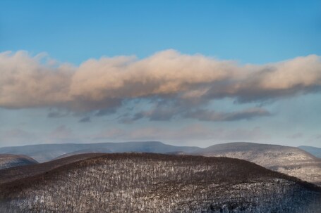 A mountainous landscape with a clear sky and fluffy clouds.