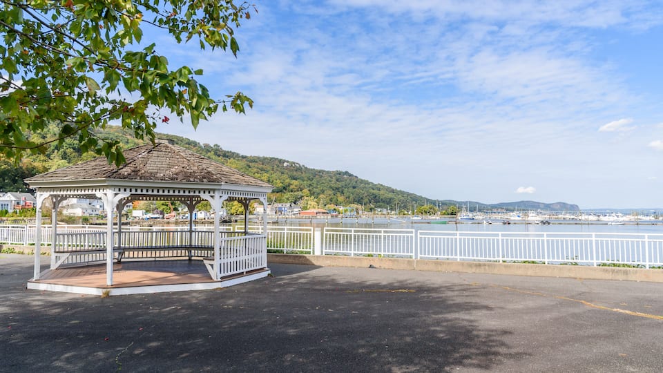 A gazebo by a waterfront with a view of boats and hills in the background.