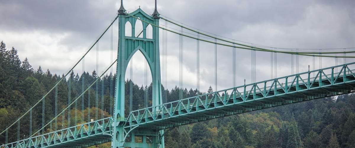 A large suspension bridge with a distinctive gothic arch design, spanning over a forested area.