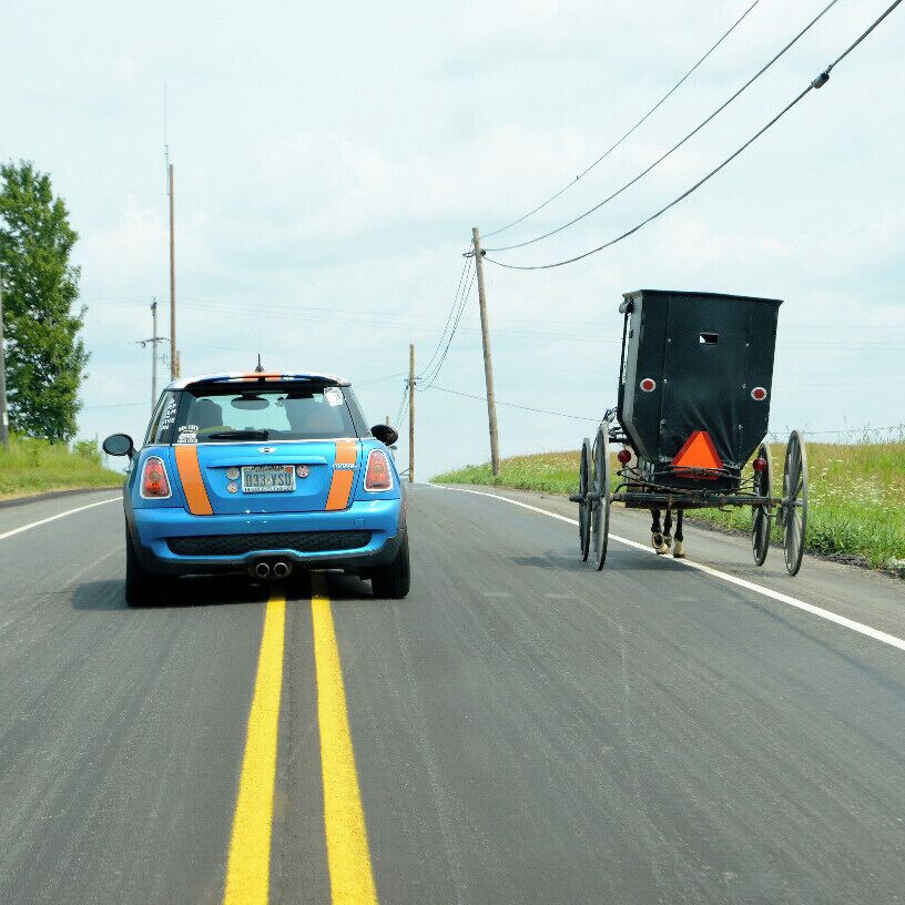 A blue car with orange stripes driving on a road with a black trailer attached.