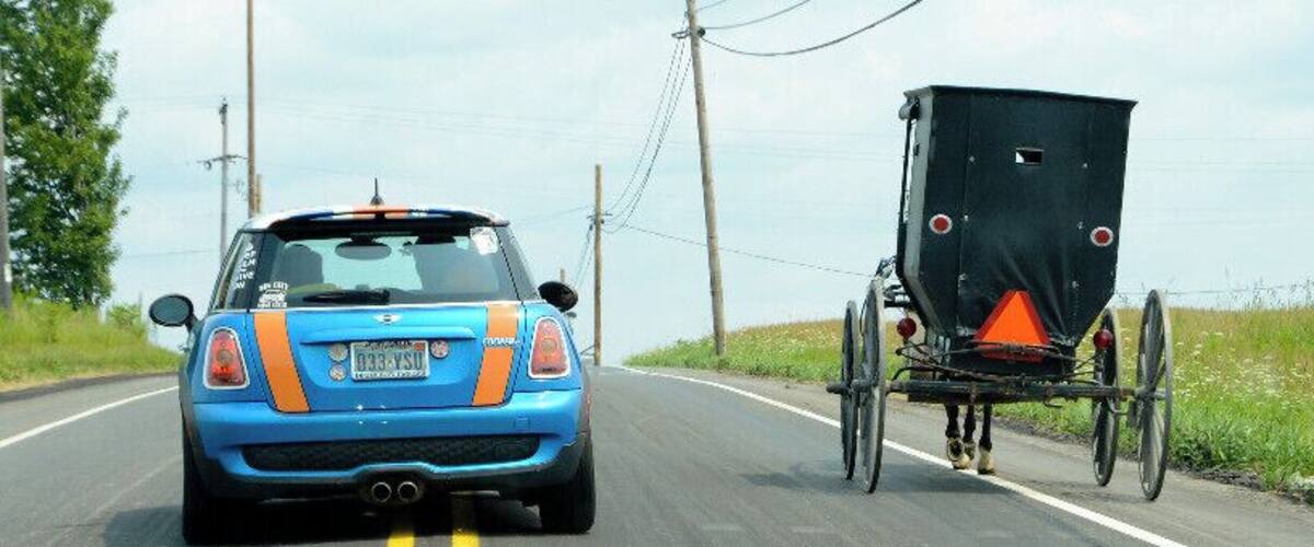 A blue car with orange stripes driving on a road with a black trailer attached.