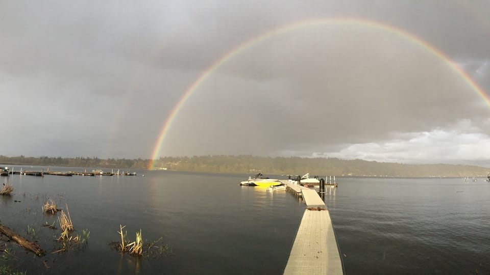 A lake with a rainbow, a dock, and a forest in the background.