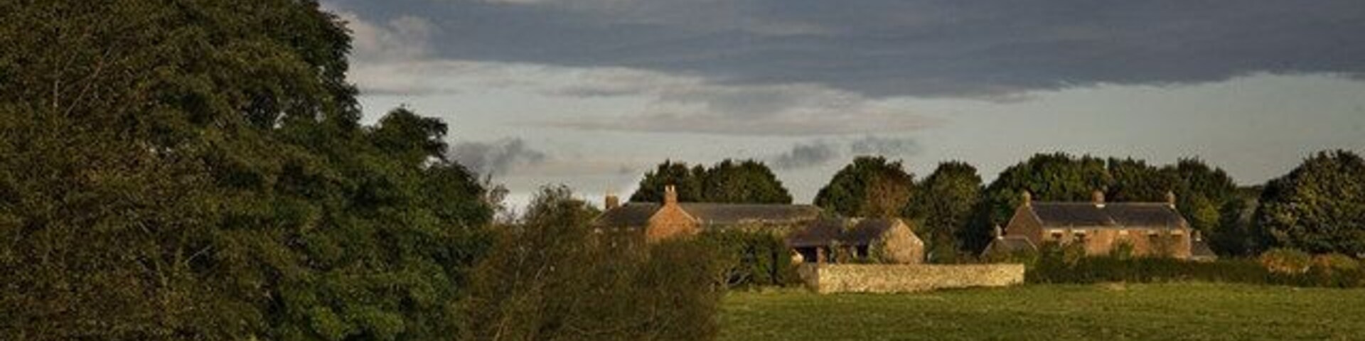 A rural landscape with a pond, trees, and stone houses.
