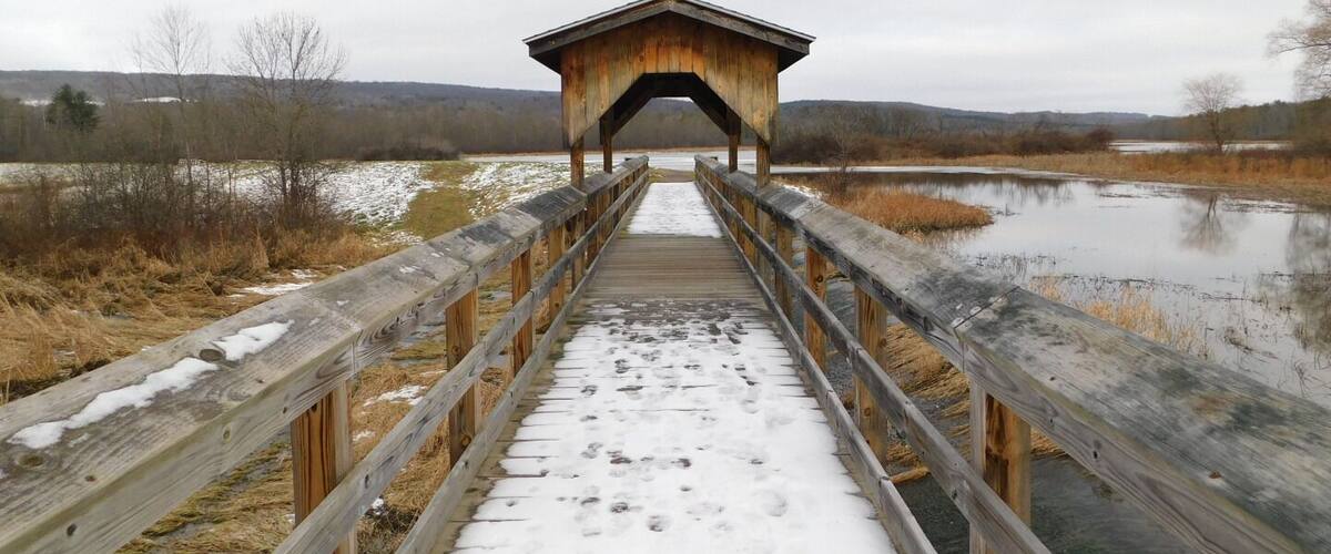 A wooden covered bridge over a frozen river with snow on the ground.