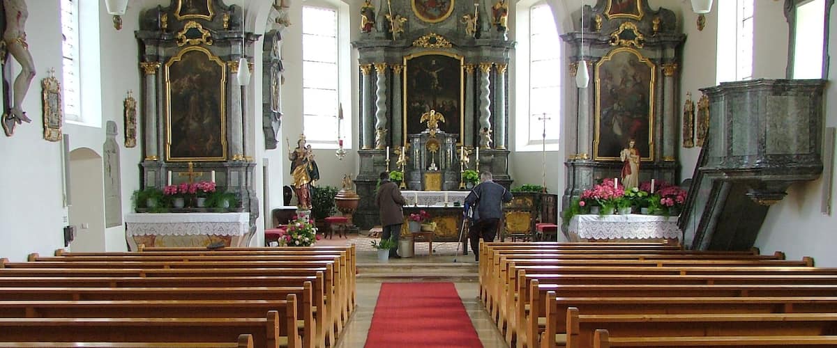 An ornate church interior with wooden pews, a red carpet, and religious statues.