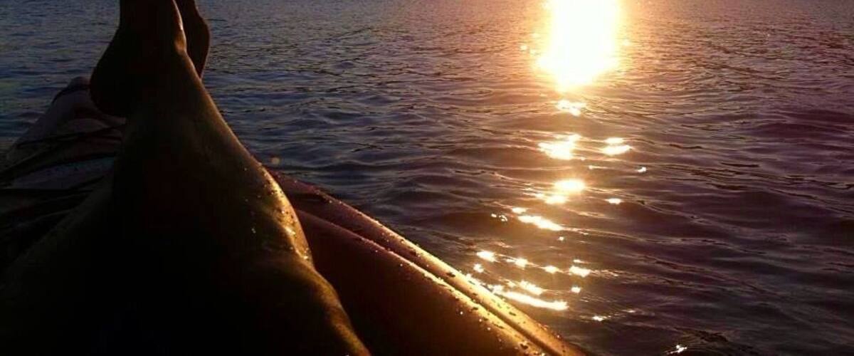 A sunset over a body of water with a silhouette of a person relaxing on a boat.