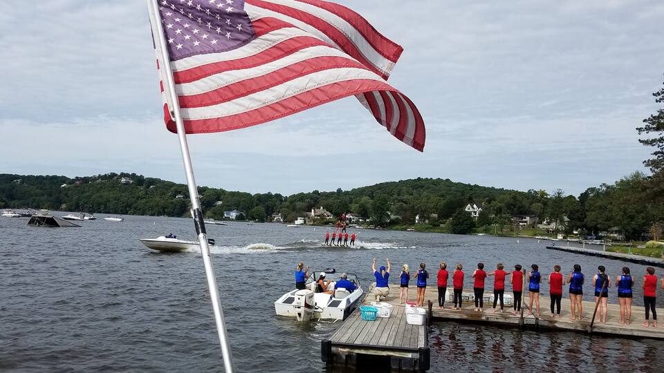 A lake with a dock, an American flag, and a group of people on a boat.