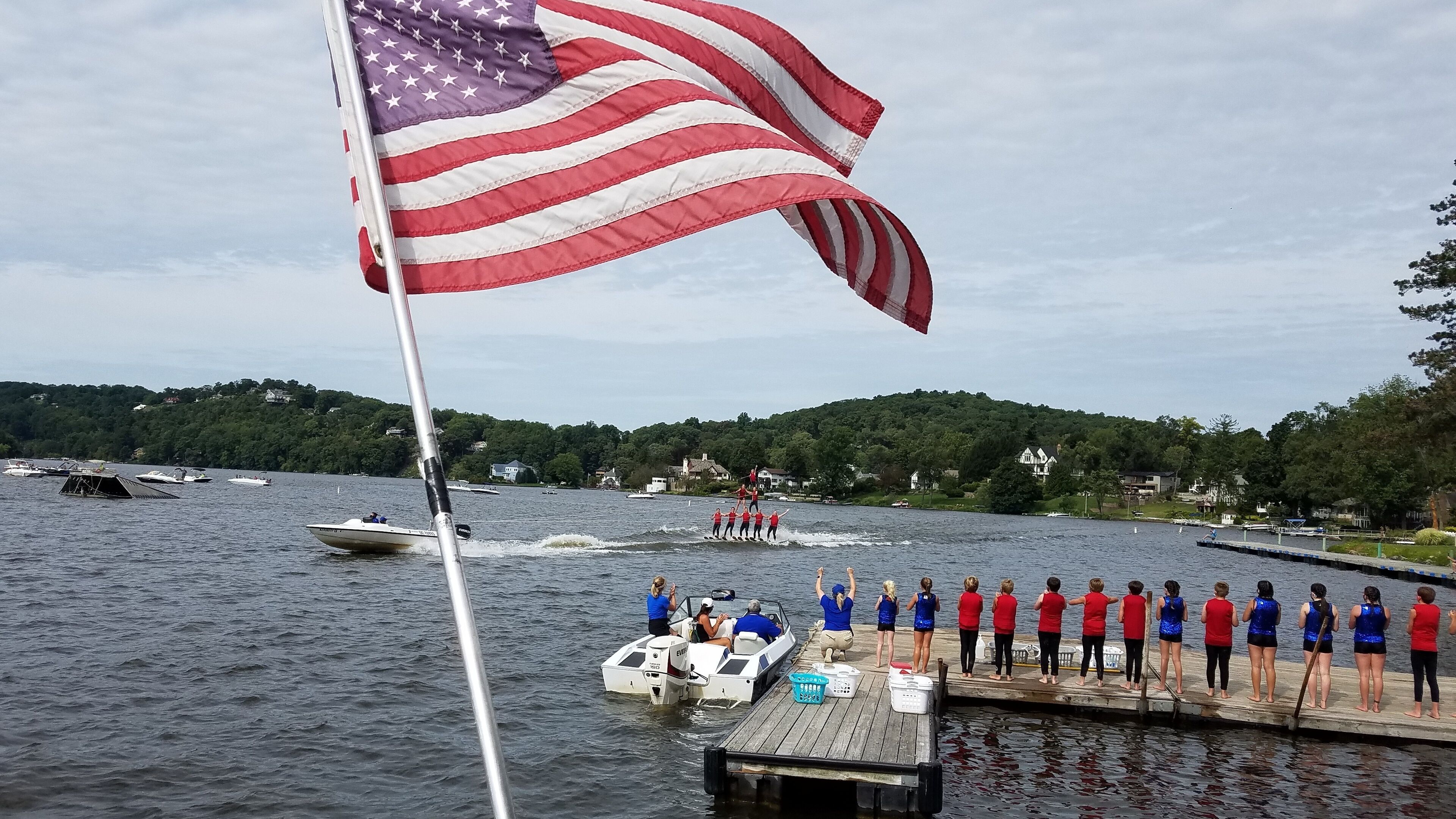 A lake with a dock, an American flag, and a group of people on a boat.