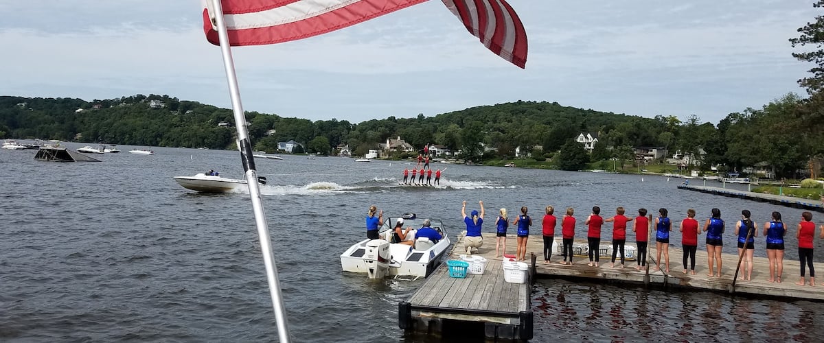 A lake with a dock, an American flag, and a group of people on a boat.