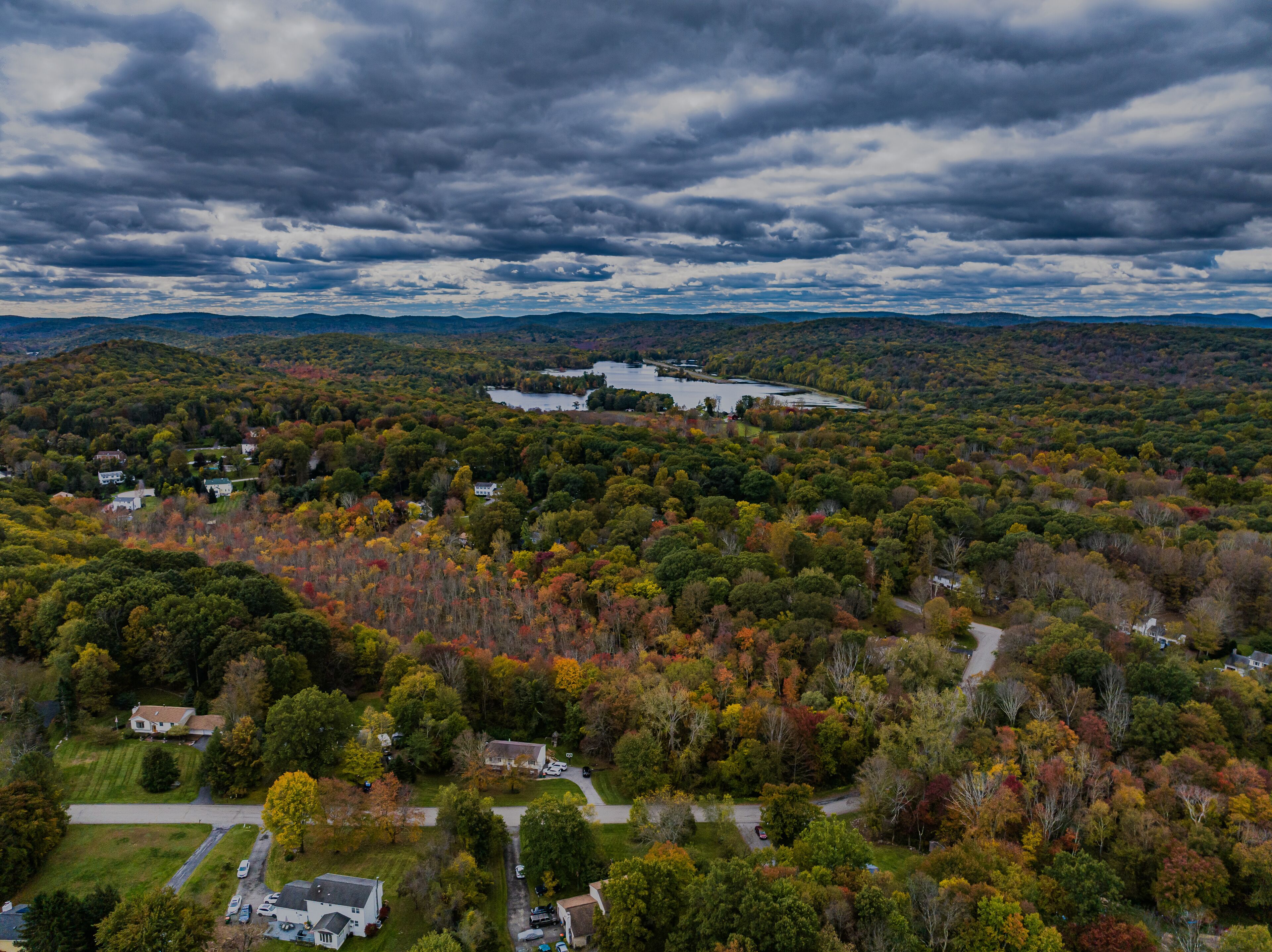 Aerial view of the countryside in Stormville, NY on a cloudy day during the colorful autumn season with a lake in view.