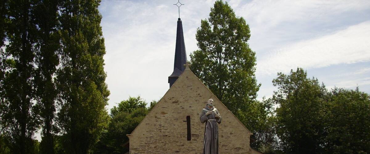 A small stone church with a statue of a religious figure in front.