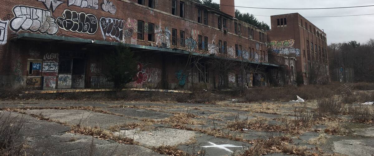 An abandoned industrial building with graffiti on the walls and a tall chimney.
