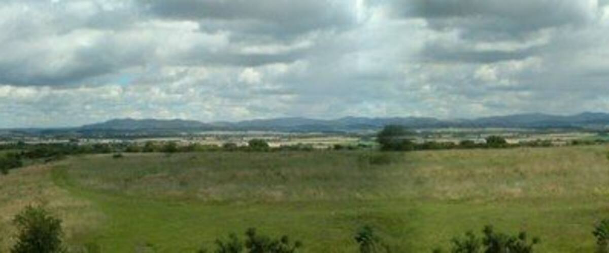 A grassy field with distant hills and a cloudy sky.