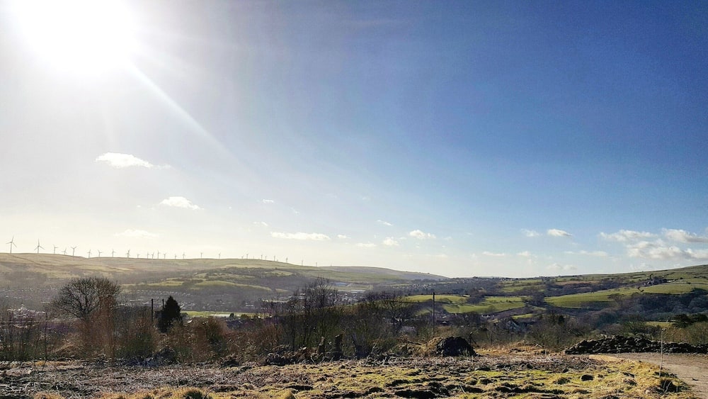 A rural landscape with wind turbines, rolling hills, and a clear sky.