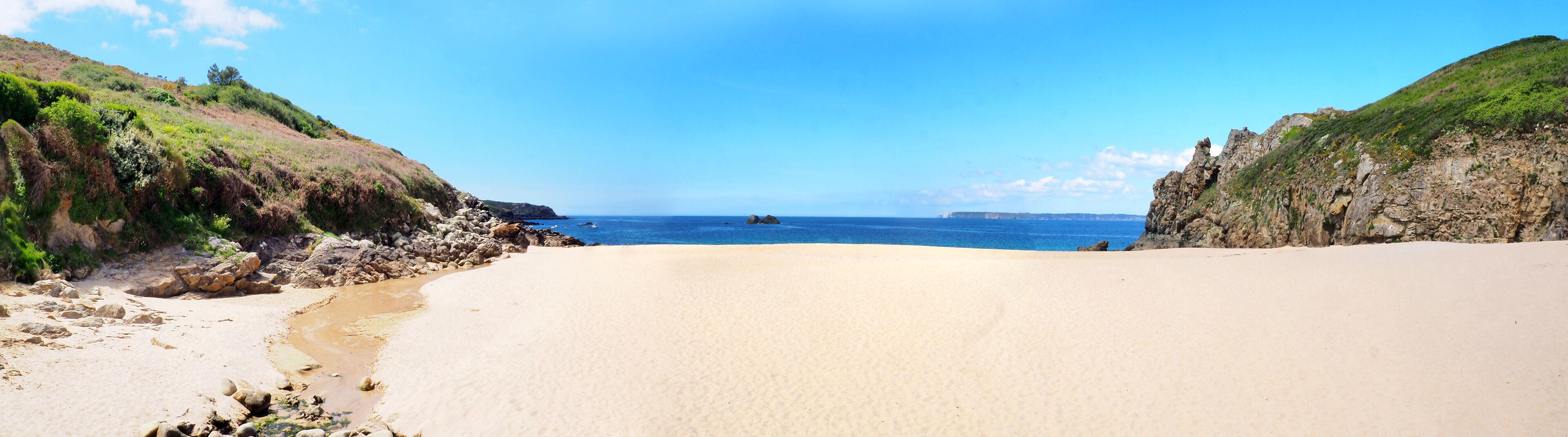 A beach with a rocky shoreline, clear blue sky, and calm sea.