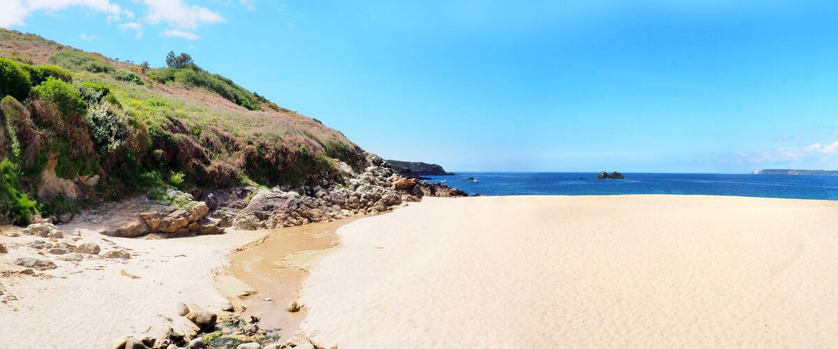 A beach with a rocky shoreline, clear blue sky, and calm sea.