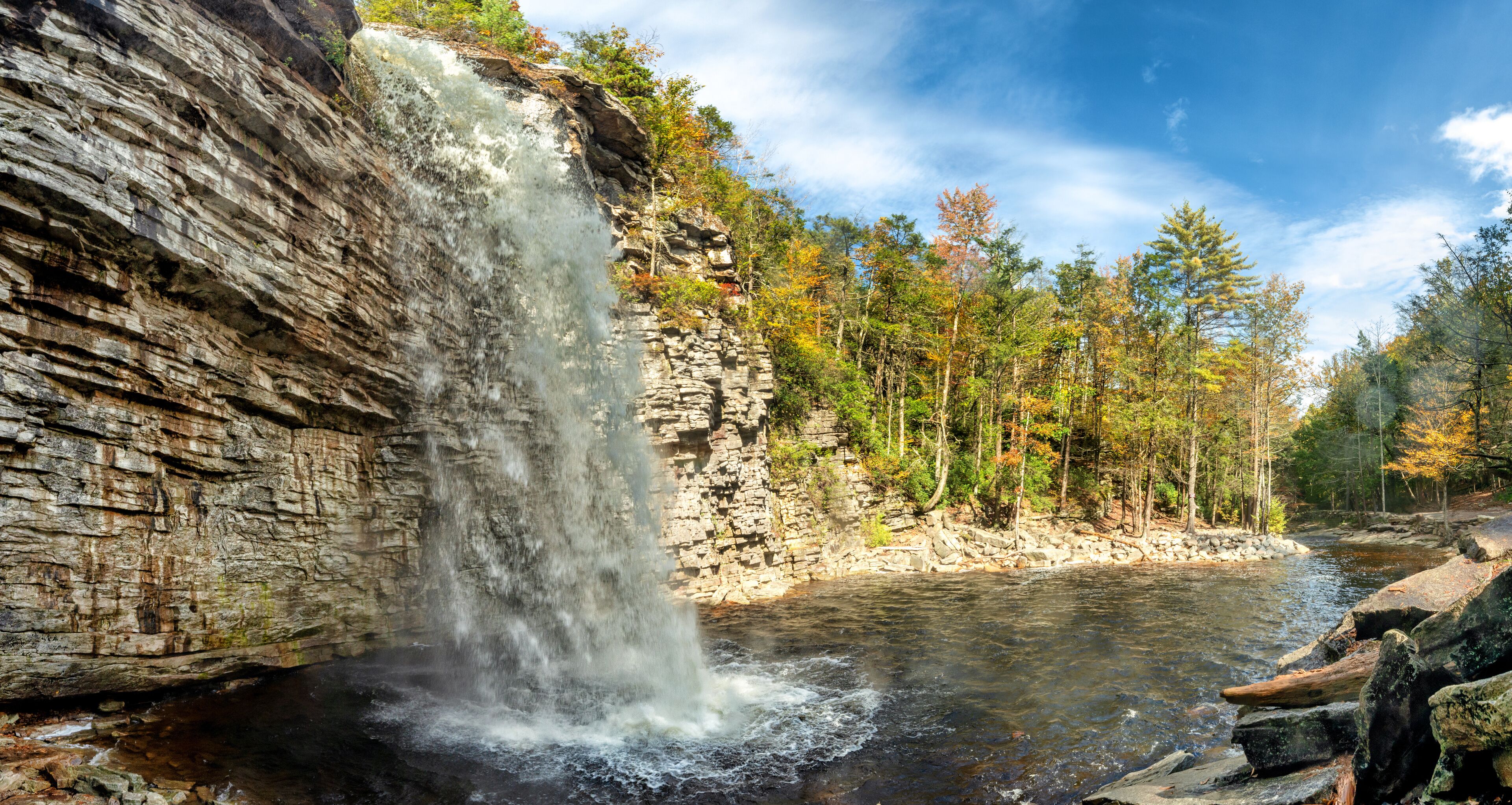 A waterfall cascading down a rocky cliff into a river surrounded by autumn-colored trees.