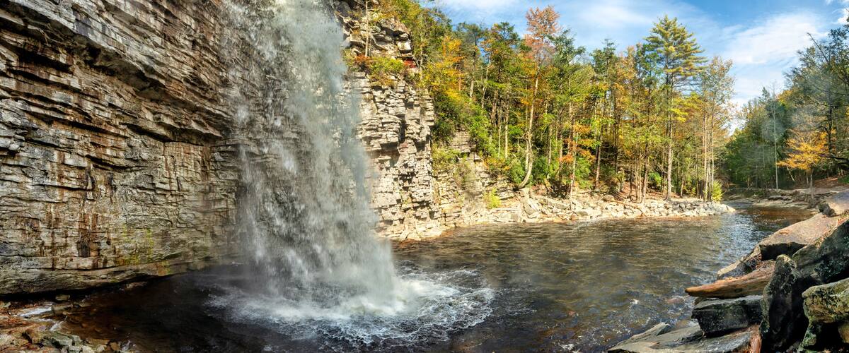 A waterfall cascading down a rocky cliff into a river surrounded by autumn-colored trees.