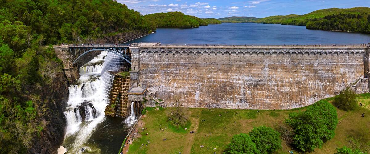 A large dam with a waterfall, surrounded by lush greenery and a calm lake.