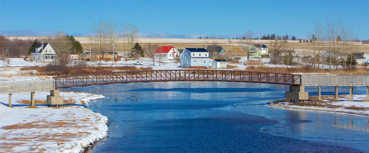 A frozen river with a wooden bridge, houses, and a clear blue sky.