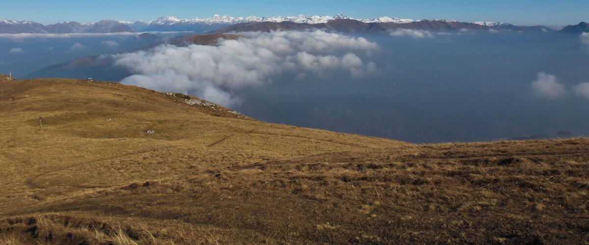 A mountain landscape with a clear sky, a valley below, and snow-capped peaks in the distance.