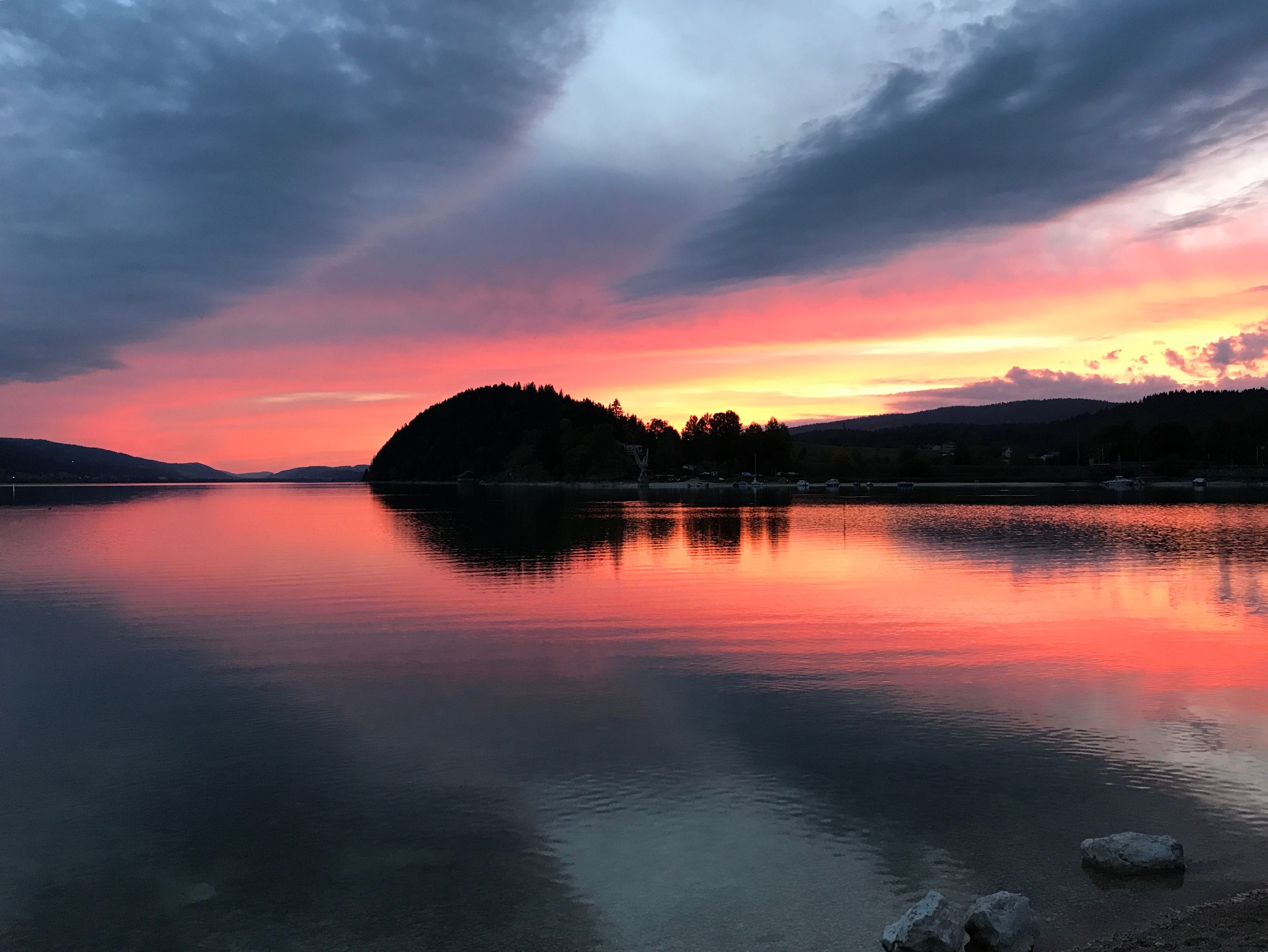 Un lago tranquilo al atardecer con una isla boscosa y colinas distantes.