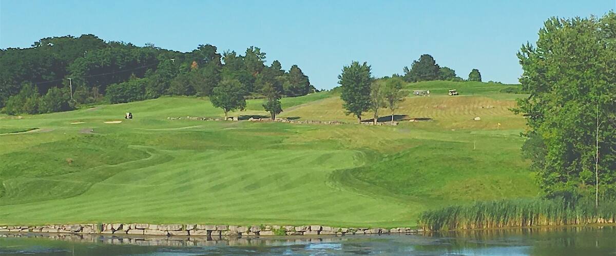 A golf course with a pond, green hills, and trees.