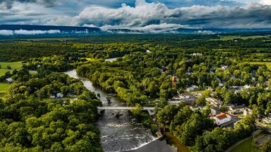 A river winding through a densely wooded area with a bridge and a small town.